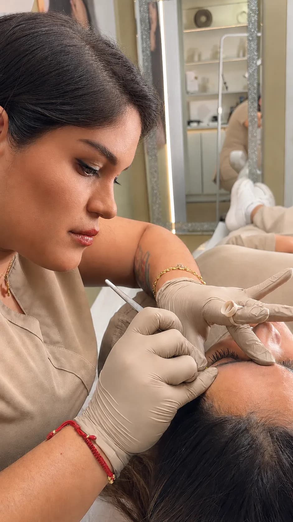 Cristina Benítez, con guantes y un instrumento fino, trabajando la ceja de una clienta recostada en el estudio.